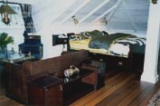 Part of a combined domestic living- and bedroom furnished with a restored 20th century original ship's king size bed, sideboard, bunk bed sofa, wall mounted bedside tables, easy chair, porthole-table and original deck-planking, as well as original lamp and newly made brass lamps.