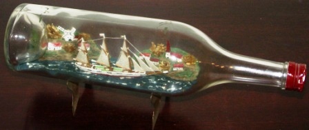 Early 20th century sailor-made ship model housed in bottle depicting a schooner with set sails. Incl metal stand.